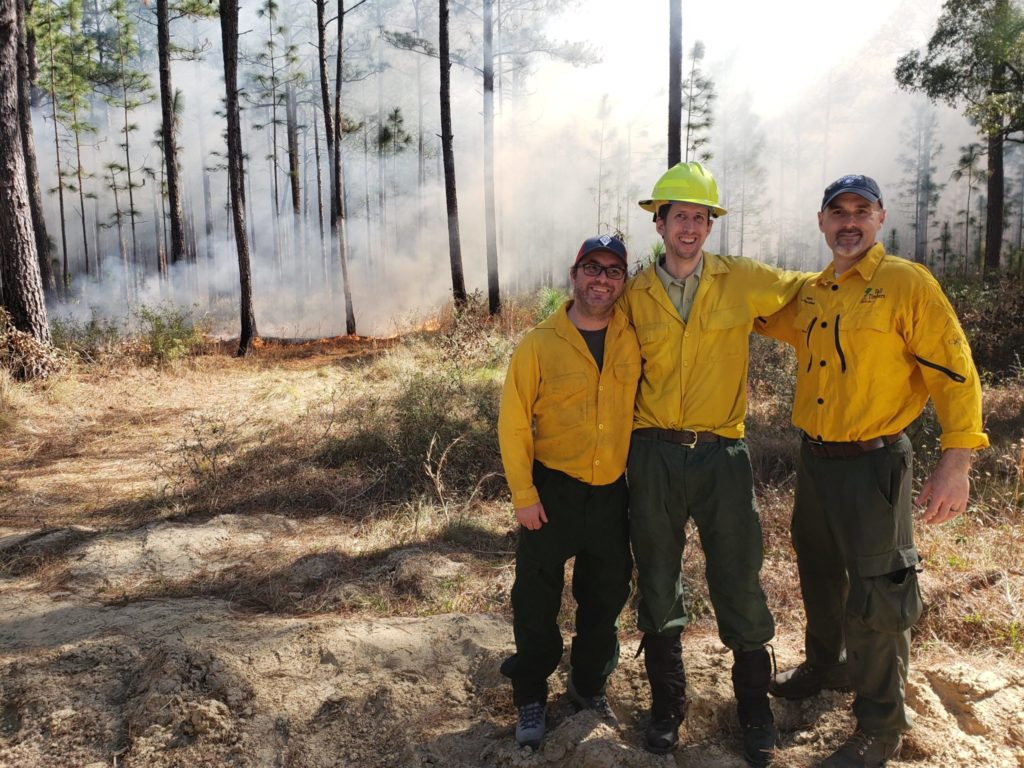 three people stand in front of a prescribed fire