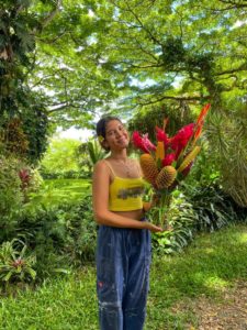 Mya Hunter standing outside surrounded by greenery. Hunter is holding a bouquet of red and yellow flowers. 