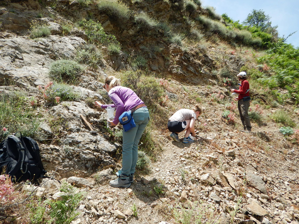 Three people conduct geoscience studies on a rocky hillside