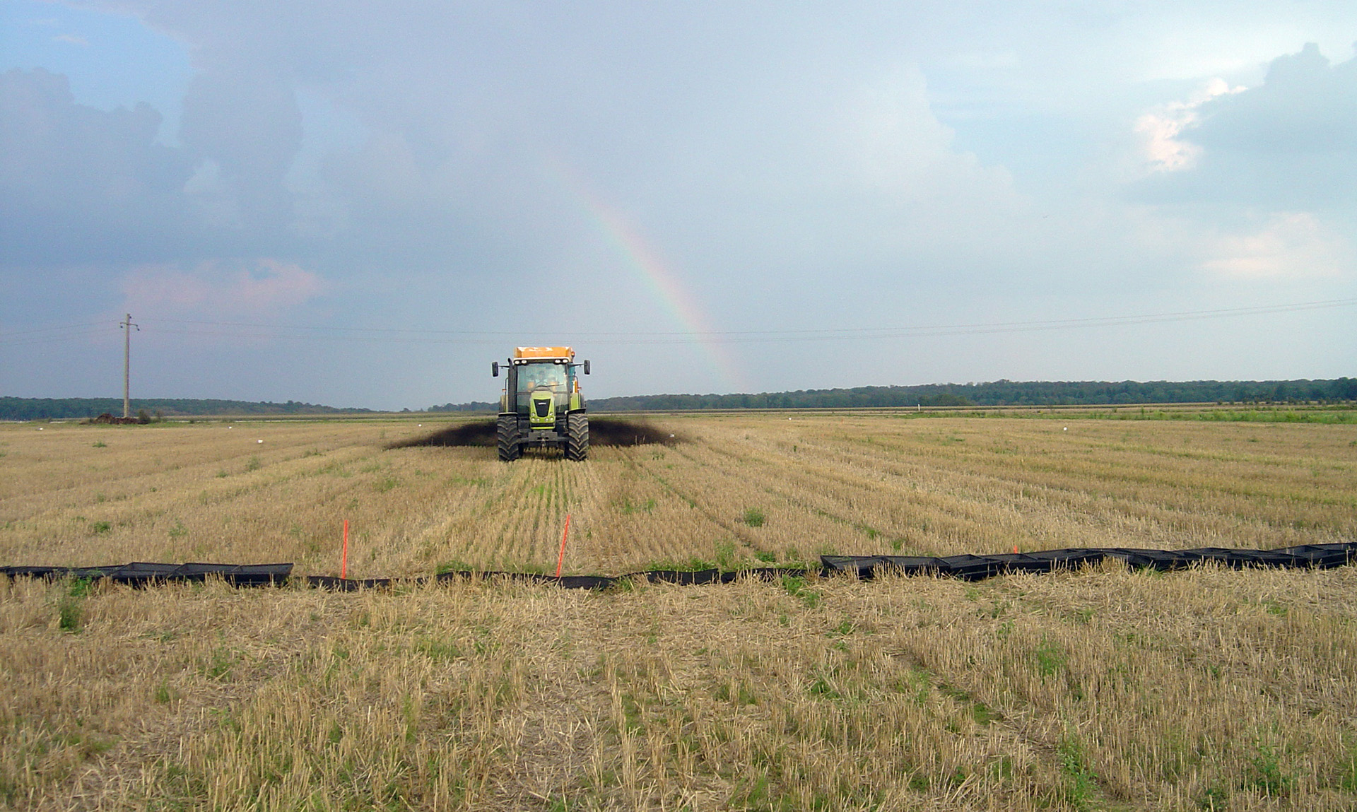 Tractor spreads compost in a field with rainbow in background