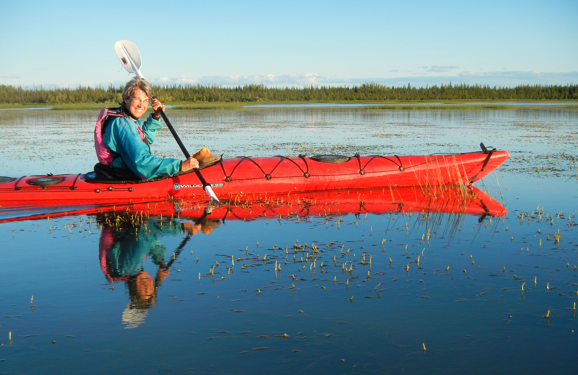 A woman kayaks on a lake in a red kayak on a sunny day.