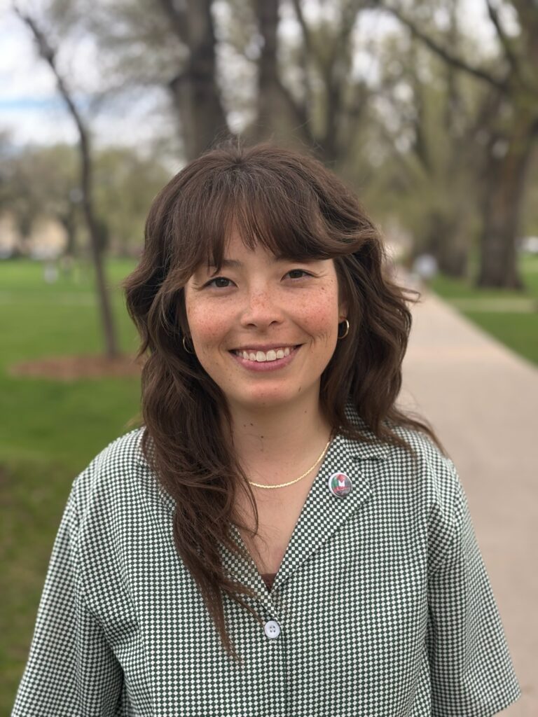 Hanna McCaslin stands posing for a headshot. She is at The Oval at Colorado State University wearing a sage green shirt.